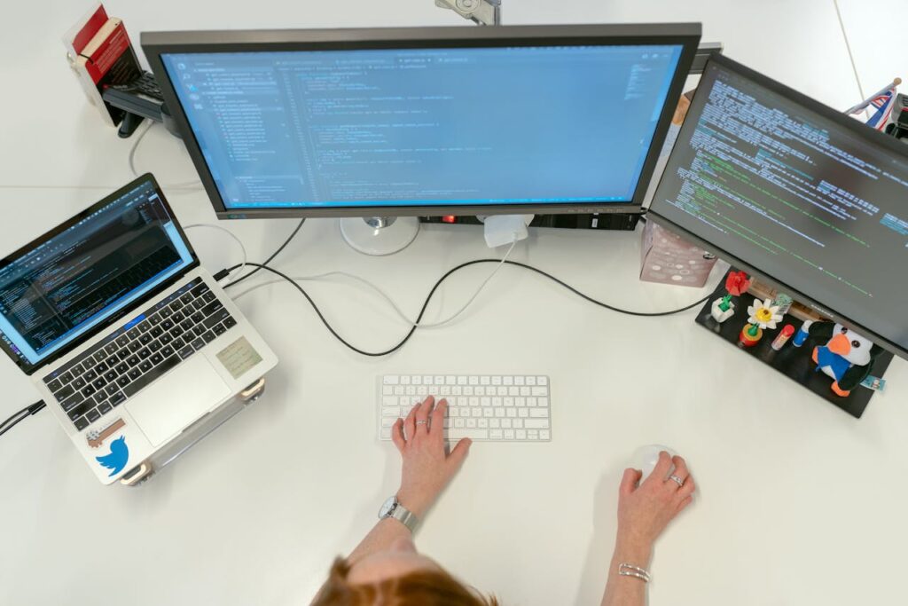 A female software engineer coding on dual monitors and a laptop in an office setting.